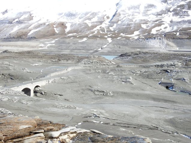The lake at the top of D1006 Col du Mont Cenis 2083m has been drained for winter maintenance. Lac du Mont Cenis is an artificial storage lake feeding two hydroelectric power plants. Col du Mont Cenis is the scenic (and free) mountain bypass of the Chambery-Turin Frejus Tunnel across the France-Italy border (one way toll €43.50). The lake is due to be refilled on Friday (29 April) but in the meantime, the original dam and water works dating from 1921 are exposed as well as – particularly – the bridge for the original pass road and customs house which marked the old border. Sadly, mere mortals won’t get to see it since the pass won’t open until 1 May at the earliest – but see Les Hydros du Mont Cenis Facebook page for more extraordinary photos.